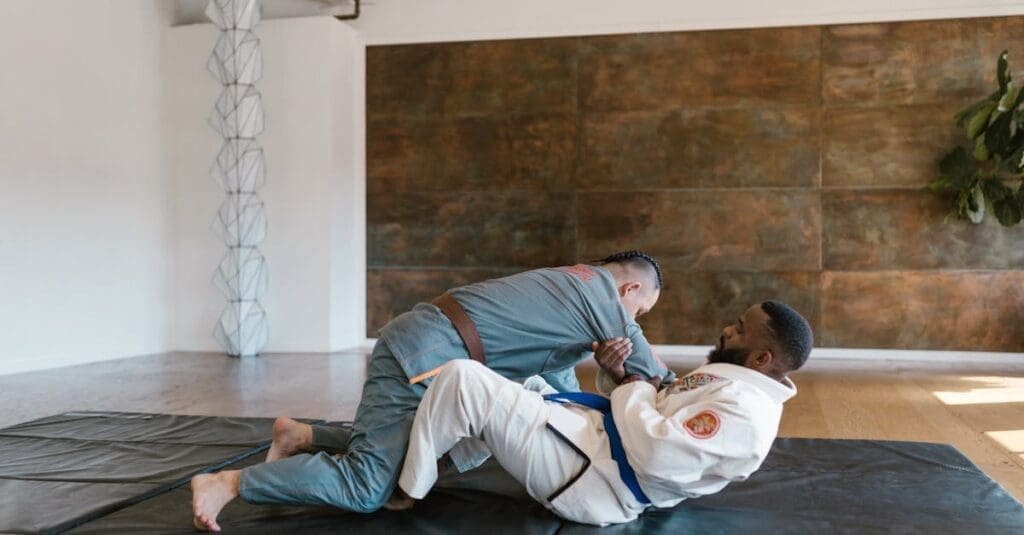 Two men participating in martial arts training for adults on a mat, practicing grappling techniques while wearing traditional Gis.