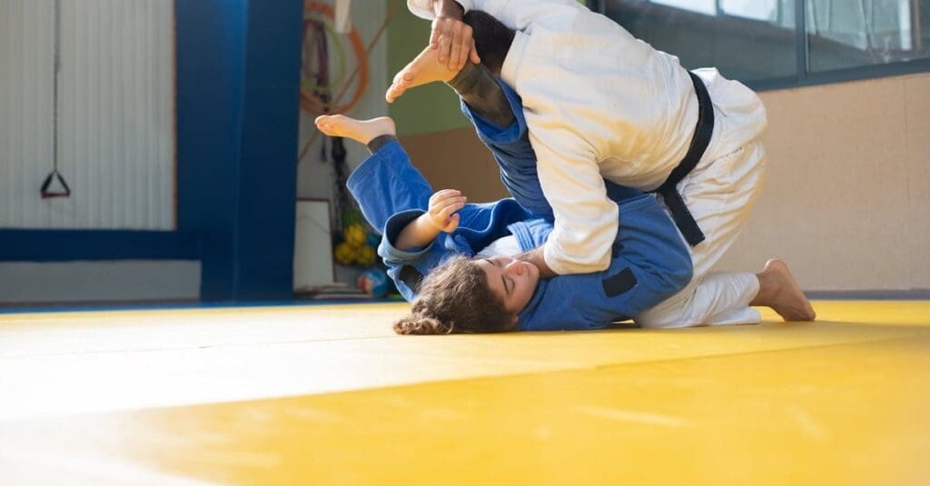 A man and a woman engaged in martial arts training for adults, practicing a ground defense technique on a yellow mat.