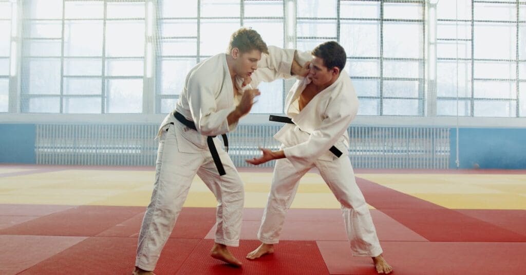 Two men wearing white uniforms and black belts sparring during a Judo or Jiu-Jitsu focused martial arts training for adults session.