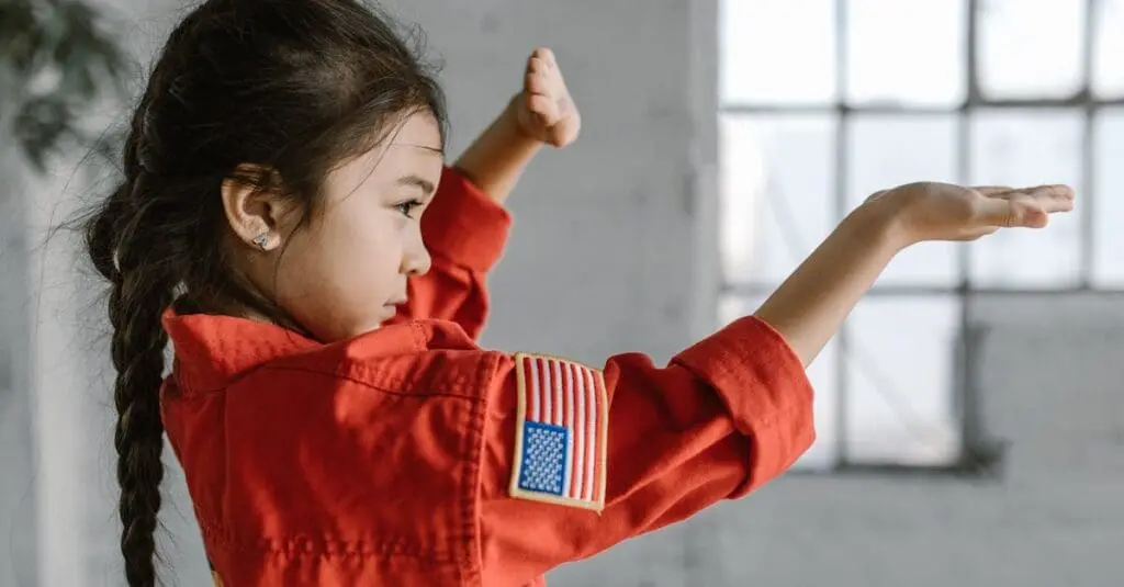 A young girl in a red martial arts uniform practicing a striking pose in a studio, highlighting preschool martial arts benefits like focus and coordination.